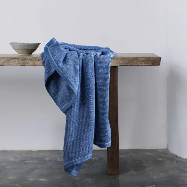 soft terry towel in ocean blue, neatly folded and styled with a small ceramic vase holding dried lavender stems